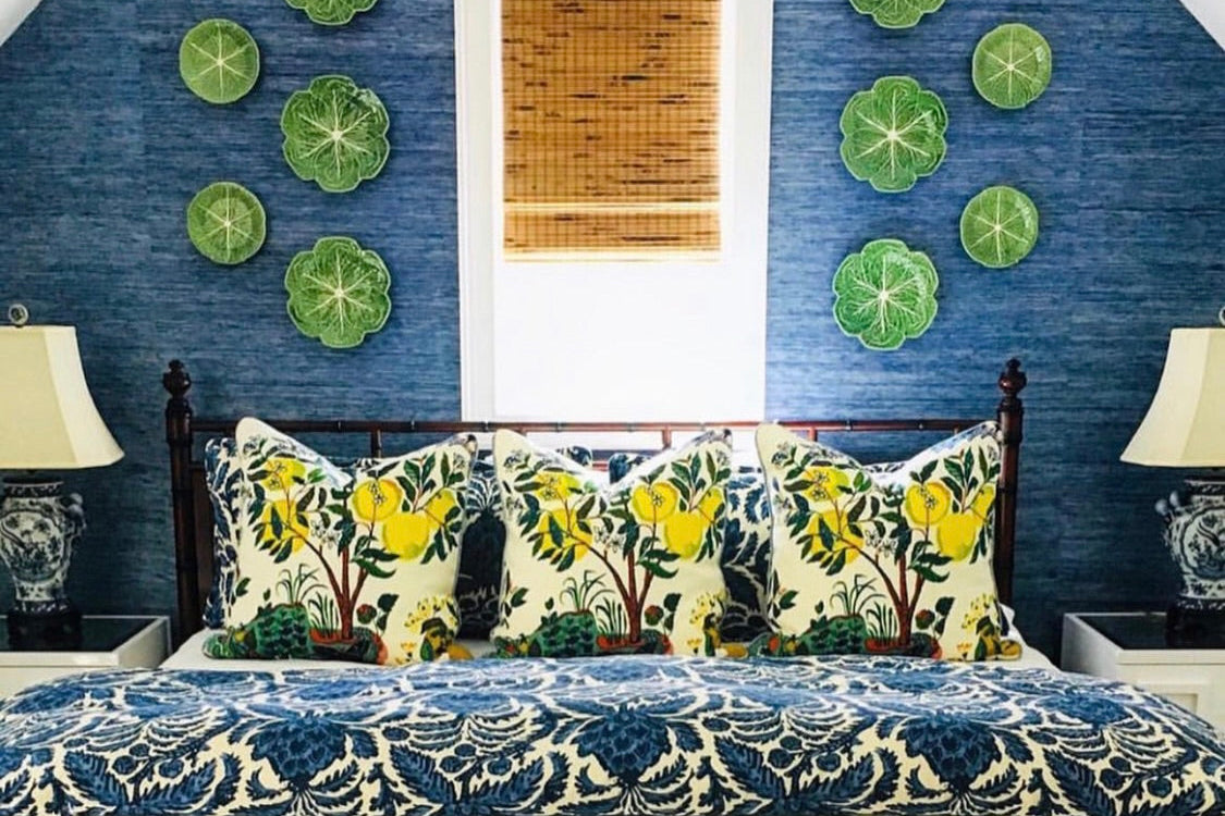 Bedroom with floral bedding and decorative pillows against a navy blue thibaut grasscloth wallpapered wall with green circular accents Schumacher Citrus Garden and Lee Jofa Fabric bedding