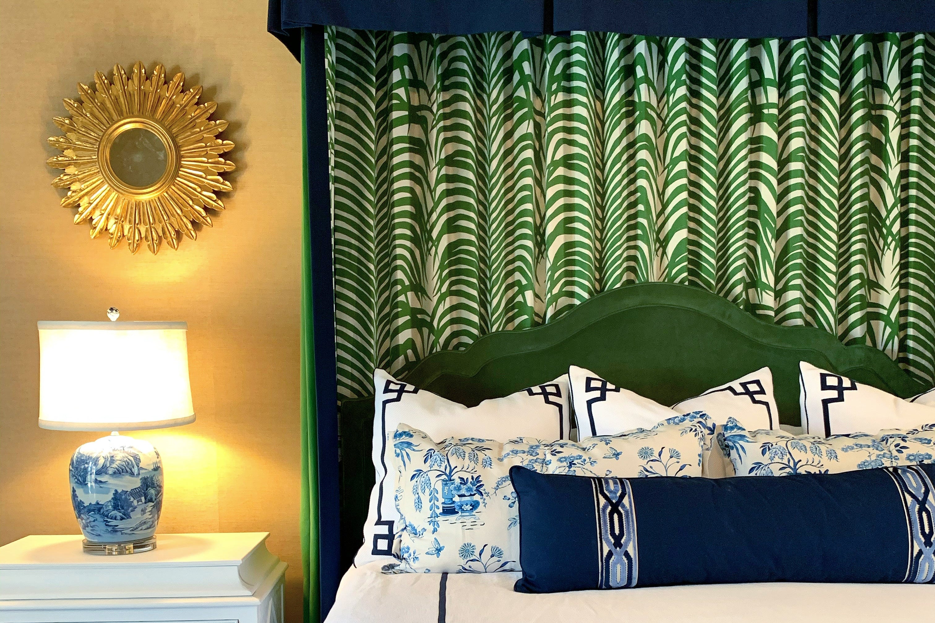 Decorative bedroom with green canopy, patterned headboard, and nightstand with lamp. Starburst mirror blue and white chinoiserie lamp, schumacher fabric and embroidered bedding canopy bed