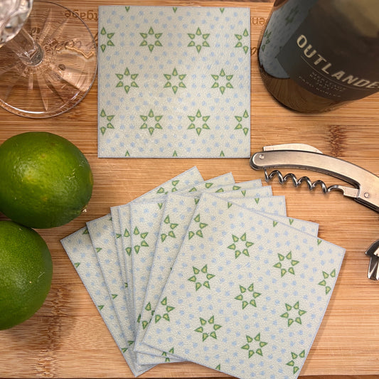 Stack of patterned napkins on a wooden surface with a bottle, corkscrew, and limes.